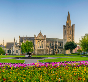 St. Patrick’s Cathedral in Dublin mit gepflegtem Rasen und Blumenbeet im Vordergrund bei klarem Himmel.