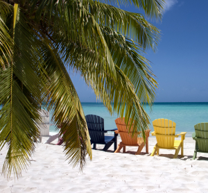 Bunte Strandst&uuml;hle im wei&szlig;en Sand unter Palmen mit Blick auf das t&uuml;rkisfarbene Meer in Jamaika.