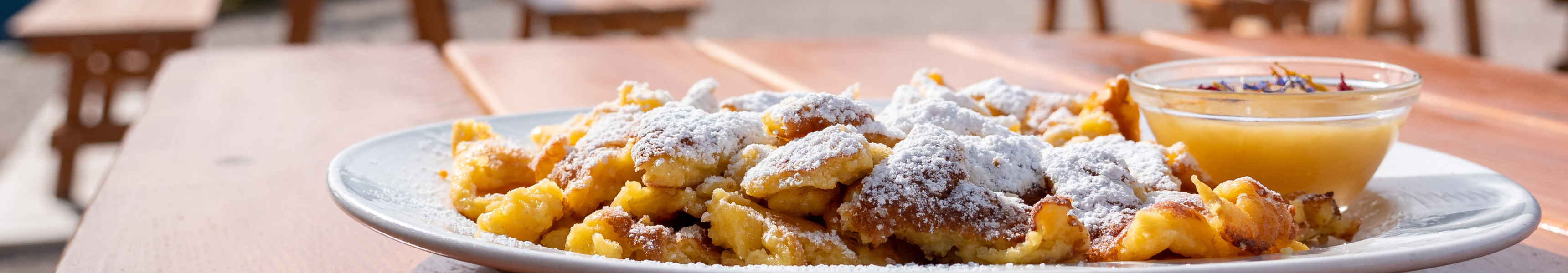 Teller mit Kaiserschmarrn und Apfelmus auf einer Bergh&uuml;tte, im Hintergrund die Dolomiten