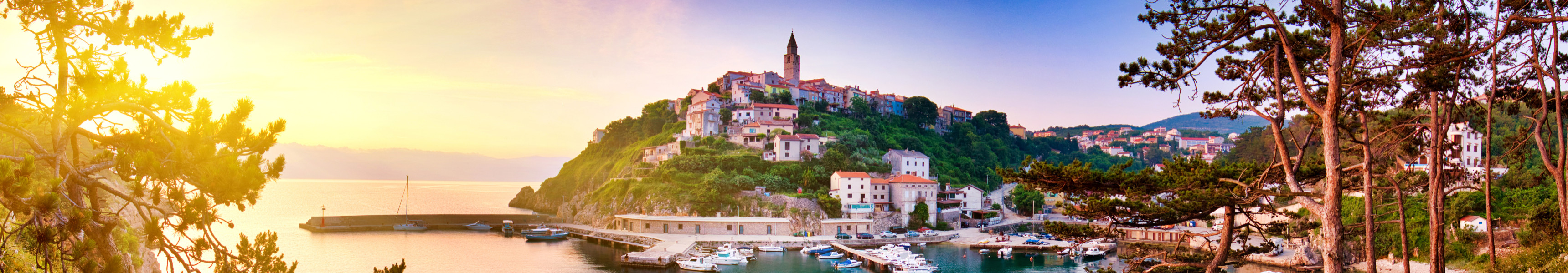 Sonnenuntergang &uuml;ber der K&uuml;stenstadt Vrbnik auf der Insel Krk in Kroatien mit Blick auf den Hafen, bunte H&auml;user und den markanten Kirchturm.