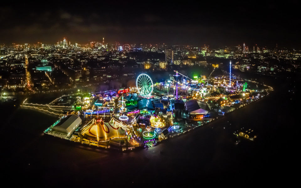 Lichtermeer des Hyde Park Winter Wonderland in London, einem der sch&ouml;nsten Weihnachtsm&auml;rkte weltweit, mit Riesenrad, festlich geschm&uuml;ckten Attraktionen und funkelnden Lichtern vor der beeindruckenden Skyline der Stadt.