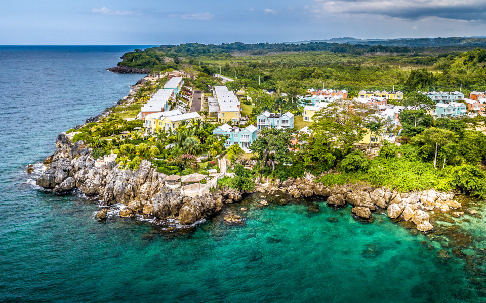 Bunte H&auml;user und gr&uuml;ne Vegetation auf einer Felsk&uuml;ste in Jamaika, umgeben vom t&uuml;rkisblauen Meer.