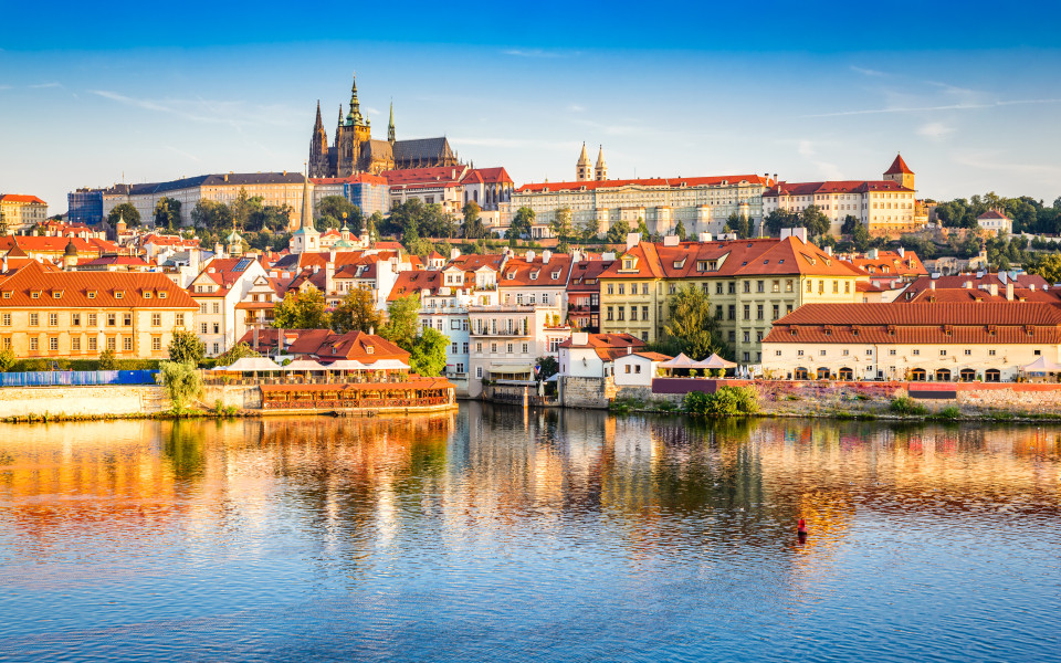Blick auf die Prager Altstadt mit dem imposanten Prager Schloss im Hintergrund und dem ruhigen Fluss Vltava im Vordergrund.