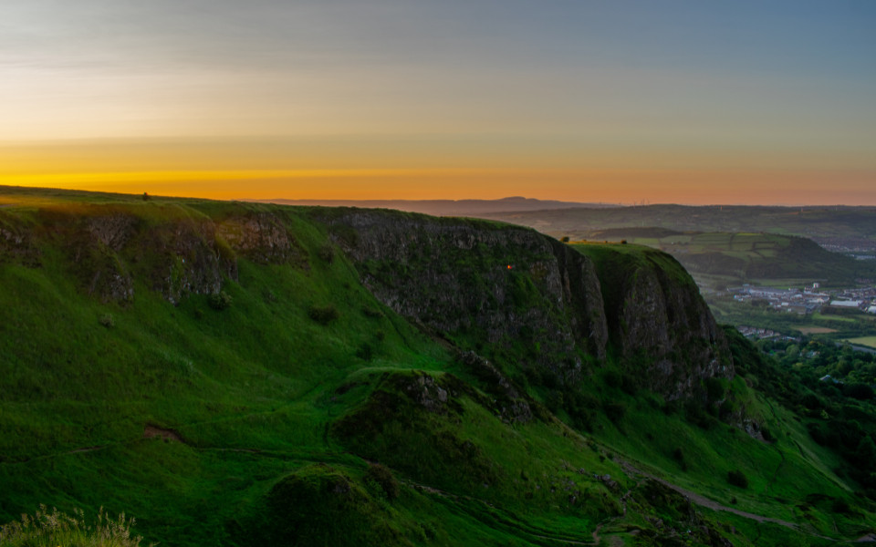 Luftaufnahme eines farbenfrohen Sonnenuntergangs im Cave Hill Country Park Belfast mit Stadt und H&uuml;gel 