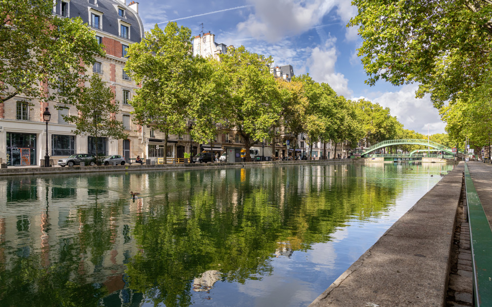 Idyllischer Canal Saint-Martin in Paris mit gr&uuml;nen B&auml;umen, Br&uuml;cke und spiegelndem Wasser